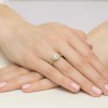 Okrągły złoty pierścionek Halo z brylantem i kamieniami bocznymi z kolekcji Dynastia, prezentowany na dłoni z różowym lakierem do paznokci produktu W0508.Z3.DIW.03