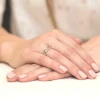 Pleciony pierścionek z białego złota z brylantami prezentowany jest na dłoni z subtelnym manicure w neutralnym kolorze produktu W0083.B3.DIW.01