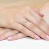 Delikatny pierścionek zaręczynowy z białego złota z brylantem osadzonym w subtelnej oprawie, prezentowany na dłoni z różowym manicure produktu W0160.B3.DIW.01