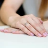 Elegancki pierścionek zaręczynowy z białego złota z motywem serca i osadzonym brylantem, prezentowany na dłoni z paznokciami pomalowanymi na jasnoróżowo produktu W0276.B3.DIW.01