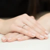 Delikatny pierścionek zaręczynowy z białego złota 585 z jednym brylantem, prezentowany na dłoni z jasnoróżowym lakierem do paznokci produktu W0387.B3.DIW.01