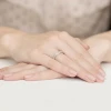 Delikatna obrączka z białego złota, wysadzana rzędem drobnych brylantów, noszona na palcu dłoni na jasnym tle produktu W0410.B3.DIW.01
