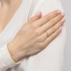 Delikatny pierścionek z białego złota z małymi brylantami w kształcie kokardki i kuleczek, prezentowany na dłoni z różowym lakierem do paznokci, produktu W0523.B3.DIW.01