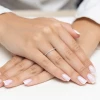 Delikatna złota obrączka z licznymi cyrkoniami prezentowana jest na dłoni z wykonanym french manicure produktu AP085-585-B