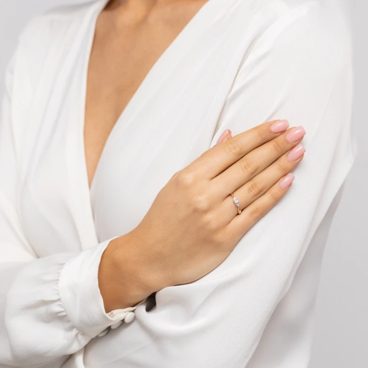 Złoty pierścionek z trzema białymi cyrkoniami osadzony na delikatnej obrączce, prezentowany na dłoni w białej bluzce produktu P180-333-B
