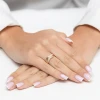 Złoty pierścionek zaręczynowy z dwoma skrzyżowanymi obrączkami, z czego jedna jest wysadzana drobnymi cyrkoniami, prezentowany na dłoni z manicure w stylu francuskim produktu P175-333-B