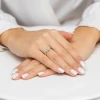 Złoty pierścionek z okrągłą niebieską cyrkonią i małymi przezroczystymi cyrkoniami, prezentowany na dłoni z białym manicure produktu P192-333-N