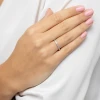 Delikatny pierścionek z białego złota wysadzany drobnymi brylantami, prezentowany na dłoni z paznokciami pomalowanymi na jasnoróżowo, na tle białej, eleganckiej bluzki produktu W0585.Z3.DIW.01