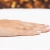 Złoty, szeroki pierścionek o ażurowym wzorze kłosów i listków, prezentowany na dłoni z paznokciami w stylu francuskiego manicure, produktu AP135-585