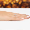 Złoty pierścionek z kwadratową niebieską cyrkonią i detalami z białych cyrkonii, prezentowany na damskiej dłoni z białym manicure na białym tle produktu P195-333-N