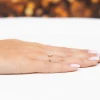 Delikatny złoty pierścionek z owalną białą cyrkonią otoczoną małymi kamieniami, prezentowany na dłoni z paznokciami w stylu francuskiego manicure produktu EP178-333-B