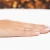 Delikatny złoty pierścionek z owalną białą cyrkonią otoczoną małymi kamieniami, prezentowany na dłoni z paznokciami w stylu francuskiego manicure produktu EP178-333-B