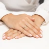 Złoty pierścionek zaręczynowy z pojedynczym brylantem osadzonym w skręconej obrączce, prezentowany na dłoni z wykonanym manicure, produktu W0669.Z3.DIW.01