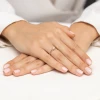 Elegancki złoty pierścionek z pojedynczym, błyszczącym diamentem prezentowany na dłoni z naturalnie wyglądającym, jasnym lakierem do paznokci produktu W0672.Z3.DIW.02