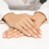 Złoty pierścionek z żółtego złota z zaplatana obrączką wysadzaną kilkoma brylantami, prezentowany na dłoni z jasnym manicure produktu W0673.Z3.DIW.01