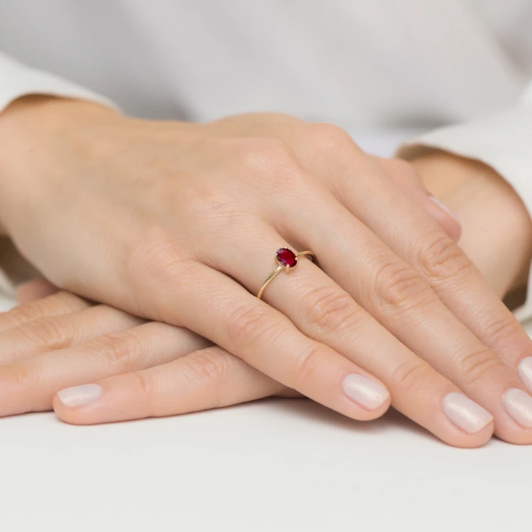 Złoty pierścionek z owalną cyrkonią w kolorze rubinowym, prezentowany na dłoni z delikatnym manicure produktu P130-333-C