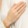Delikatny złoty pierścionek z okrągłym białym kamieniem osadzonym w oprawie typu bezel, prezentowany na dłoni kobiety na białym tle produktu P150-333-B