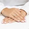 Elegancki pierścionek zaręczynowy z białego złota, zdobiony centralnie osadzonym kwadratowym diamentem Princessa oraz dodatkowymi brylantami, prezentowany na dłoni produktu W0591.B3.DIW.01
