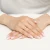 Złoty pierścionek z centralnie osadzoną białą owalną cyrkonią w ozdobnej, ażurowej oprawie, prezentowany na dłoniach z manicure francuskim produktu AP205-585-B