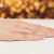 Delikatny złoty pierścionek z niewielką różową cyrkonią w centrum, prezentowany na dłoni z idealnie wykonanym french manicure, na subtelnym tle produktu W0045.Z6.ZIR.01
