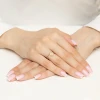 Delikatny złoty pierścionek z motywem kwiatka koniczynki wysadzanego cyrkoniami, prezentowany na dłoni z paznokciami w stylu francuskiego manicure, produktu AP201-585-B