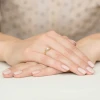 Złoty pierścionek mijanka z pojedynczym, błyszczącym diamentem laboratoryjnym, prezentowany na dłoni z subtelnym manicure produktu W0163.Z3.LDW.03