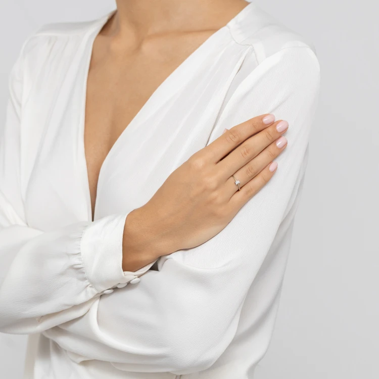 Elegancki pierścionek z białego złota z centralnie osadzonym prostokątnym diamentem, prezentowany na dłoni modelki odzianej w białą bluzkę, produktu W0592.B3.DIW.01