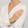 Delikatny pierścionek z białego złota w kształcie kwiatka, zdobiony subtelnymi diamentami, prezentowany na dłoni kobiety w eleganckiej białej bluzce produktu W0627.B3.DIW.01