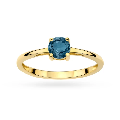 Żółte złoto tworzy delikatną obrączkę, na której osadzono okrągły, głęboko niebieski topaz London Blue, prezentowany na białym tle produktu W0656.Z3.TOL.01