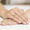 Delikatny pierścionek zaręczynowy z białego złota z pojedynczym brylantem, prezentowany na dłoni z jasnym manicure produktu W0228.B3.DIW.02