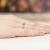 Białe złoto z pojedynczym, okrągłym, przezroczystym kamieniem osadzonym na delikatnej obrączce, prezentowany na dłoni kobiety z manicure w cielistym kolorze, produktu W0404.B3.DIW.01