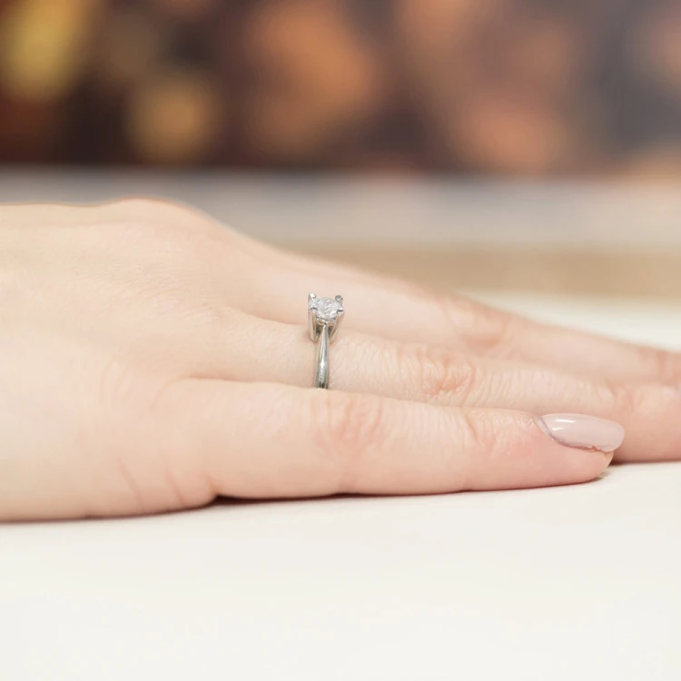 Białe złoto z pojedynczym, okrągłym, przezroczystym kamieniem osadzonym na delikatnej obrączce, prezentowany na dłoni kobiety z manicure w cielistym kolorze, produktu W0404.B3.DIW.01