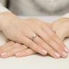Elegancki pierścionek zaręczynowy z białego złota z pojedynczym brylantem prezentowany jest na dłoni z paznokciami pomalowanymi na pastelowy róż produktu W0482.B3.DIW.02