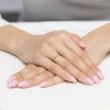 Złoty pierścionek z pojedynczą, subtelną cyrkonią w nietypowej, falistej oprawie, prezentowany na dłoni o naturalnym odcieniu skóry z delikatnym, różowym manicure produktu P218-333-B