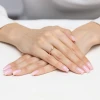 Delikatny złoty pierścionek z pojedynczą, błyszczącą cyrkonią, prezentowany na dłoni z jasnoróżowym, kwadratowym manicure produktu P219-333-B