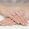 Delikatny pierścionek z różowego złota z pojedynczym diamentem laboratoryjnym otoczonym mniejszymi kamieniami, prezentowany na dłoni z pomalowanymi na jasnoróżowo paznokciami produktu W0435.R3.LDW.01