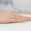 Delikatny pierścionek z różowego złota z pojedynczym diamentem laboratoryjnym na środku i mniejszymi diamentami laboratoryjnymi wysadzanymi wzdłuż obrączki, prezentowany na dłoni produktu W0435.R3.LDW.01
