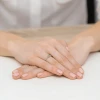 Pierścionek z białego złota z brylantami i centralnym, szmaragdowym kamieniem, prezentowany na dłoni produktu W0435.B3.EMG.01