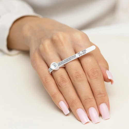 Uniwersalna miarka multisizer w kolorze białym, bez kamieni, z widocznym nadrukiem podziałki i tekstu, prezentowana na dłoni z różowym, zadbanym manicure produktu A087