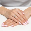 Delikatny złoty pierścionek z centralnie osadzonym niebieskim kamieniem w kształcie łezki oraz dwoma małymi białymi kamieniami po bokach, prezentowany na dłoni z jasnym manicurem produktu AP223-333-BN