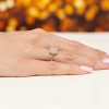 Złoty pierścionek z kwadratową oprawą wypełnioną mniejszymi diamentami i otoczoną większymi, prezentowany na dłoni produktu W0574.Z3.DIW.01