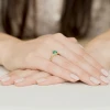Wykwintny pierścionek z żółtego złota z owalnym szmaragdem otoczonym brylantami, prezentowany na dłoni z delikatnym manicure, produktu W0308.Z3.EMG.01.