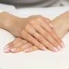 Złoty pierścionek z niewielką okrągłą cyrkonią prezentowany na dłoni z paznokciami w stylu francuskiego manicure produktu AP236-333-B