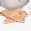 Elegancki złoty pierścionek zaręczynowy z centralnie osadzonym diamentem po bokach otoczonym dwoma szafirami, prezentowany na dłoni produktu W0711.Z3.DIW.01