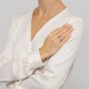 Delikatny pierścionek z białego złota w kształcie koniczynki wysadzanej drobnymi brylantami, prezentowany na dłoni modelki ubranej w białą koszulę produktu W0696.B3.DIW.01