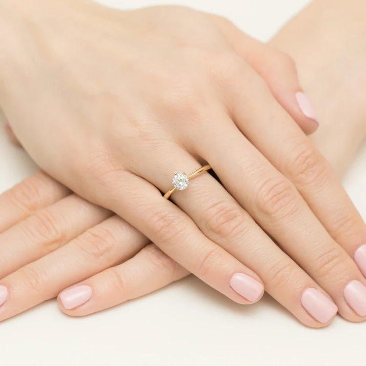 Elegancki pierścionek z żółtego złota z centralnie osadzonym, okrągłym diamentem laboratoryjnym prezentowany jest na kobiecej dłoni z różowym manicure produktu W0553.Z3.LDW.03