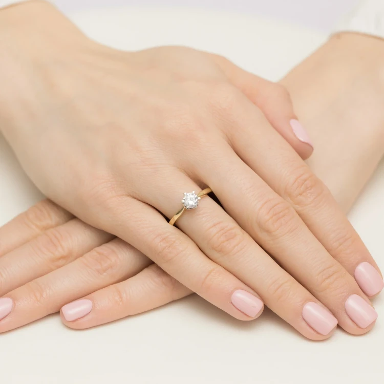 Elegancki pierścionek z żółtego złota z centralnym, okrągłym diamentem laboratoryjnym otoczonym mniejszymi diamentami laboratoryjnymi, prezentowany na dłoni z paznokciami w pastelowym kolorze produktu W0539.Z3.LDW.03