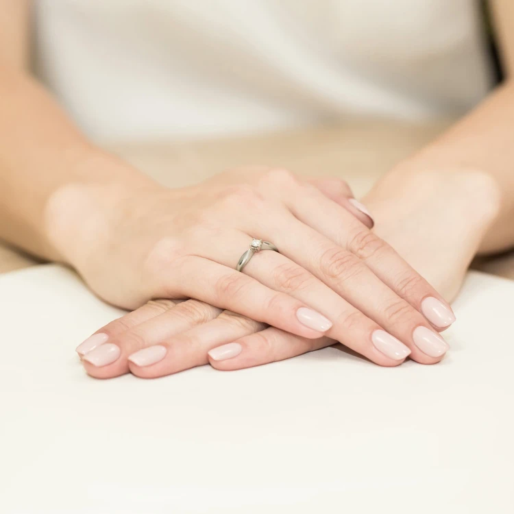 Elegancki pierścionek zaręczynowy z białego złota z pojedynczym brylantem 0,12ct, prezentowany na dłoni z jasnoróżowym lakierem do paznokci, produktu W0171.B3.DIW.01
