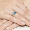 Pierścionek z białego złota z niebieskim topazem i białymi diamentami, prezentowany na dłoni z jasnoróżowym lakierem do paznokci produktu W0148.Z3.TOB.01