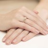 Elegancki pierścionek zaręczynowy z białego złota z centralnie osadzonym brylantem i mniejszymi brylantami wysadzanymi wzdłuż obrączki, prezentowany na dłoni z naturalnym manicure produktu W0052.B3.DIW.02